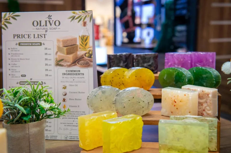 The OLIVO price list beside rows of handmade soaps at the kiosk