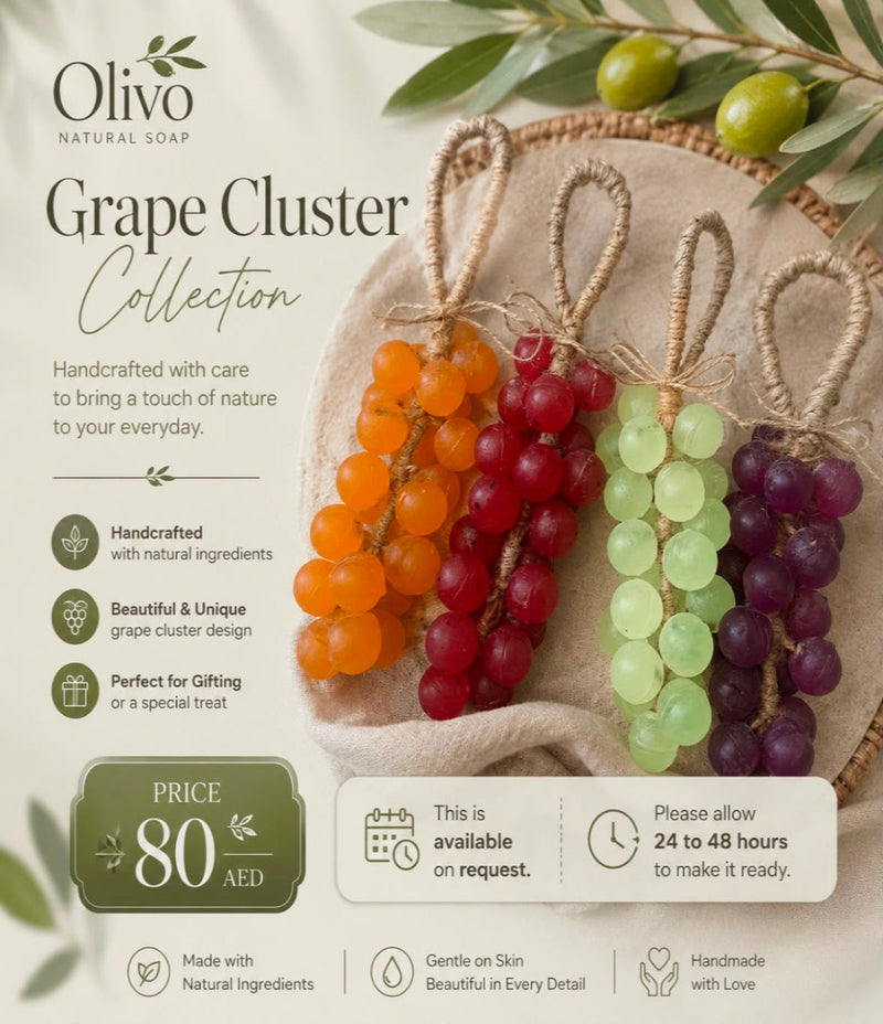 Promotional graphic for the Olivo Natural Soap Grape Cluster Collection, showing three handmade grape cluster soap ornaments in shades of orange, red, and purple, hanging from twine loops on a beige fabric background.